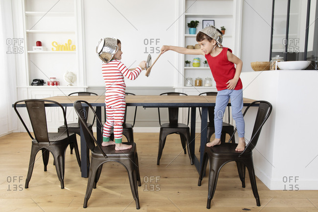 Young boys playing swords with wooden utensils in kitchen