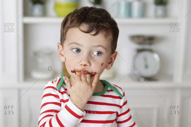 Young boy with messy chocolate face licking fingers
