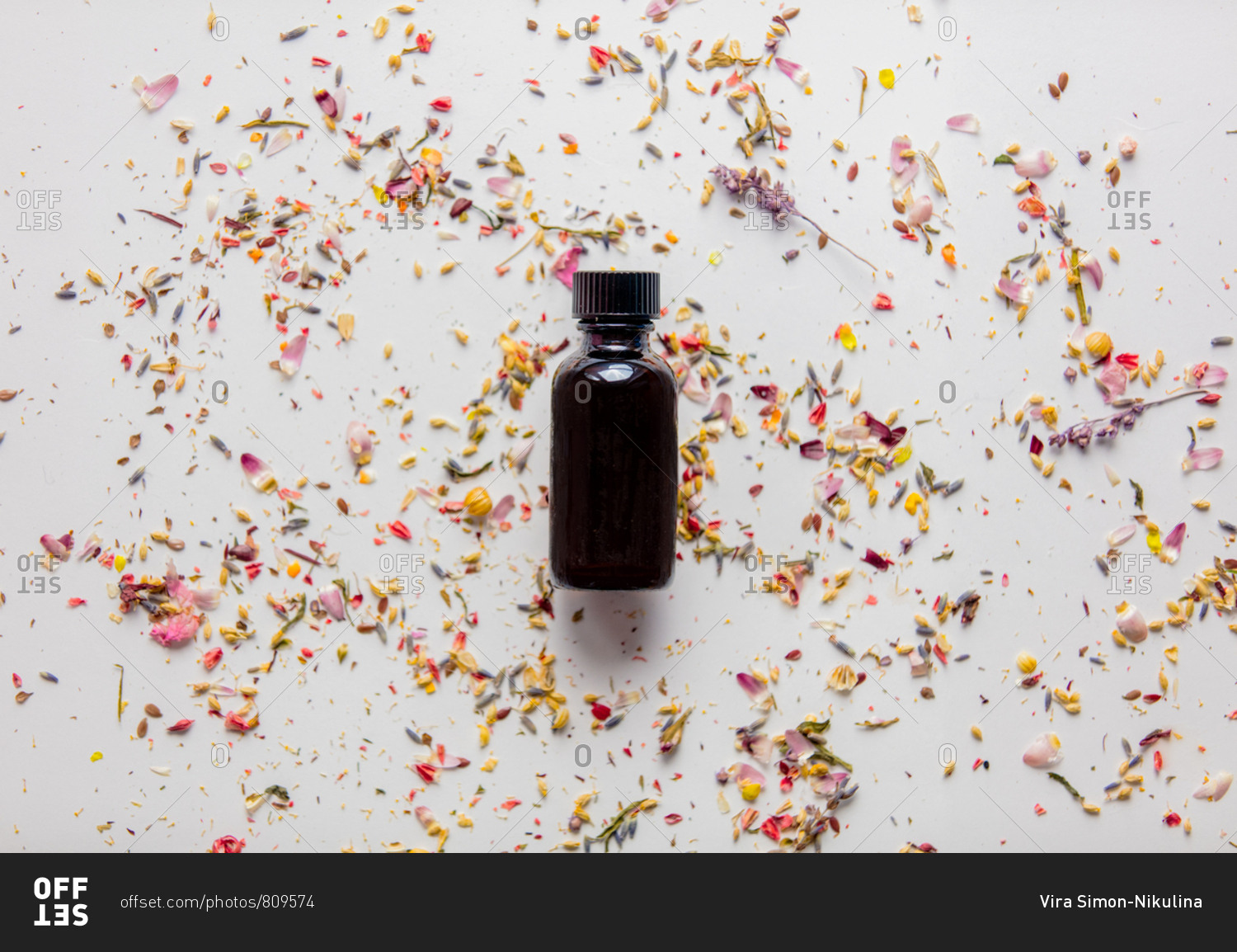 Black glass bottle with lavender flower petals on a white background