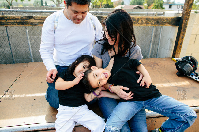 Children act silly while sitting on half pipe with their parents