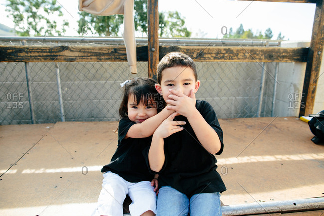Siblings covering brothers mouth while sitting on half pipe
