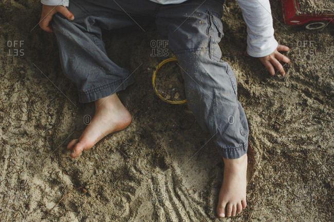 The bottom half of a small boy playing barefoot in a sandbox