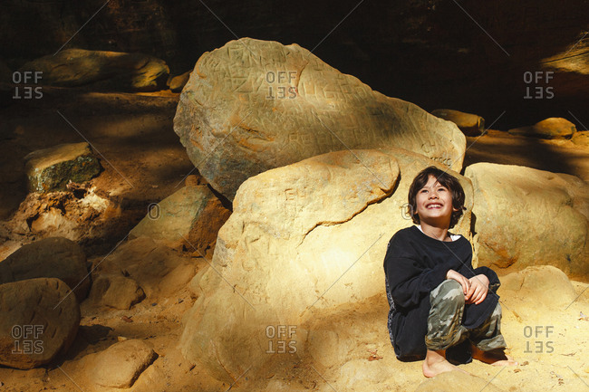 A happy boy leans barefoot against rock outcropping in golden light