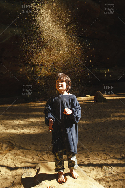 A small barefoot child throws golden sand into the air in sunlit gorge