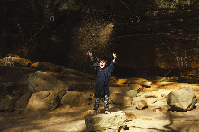 A small boy shouts with joy and throws sunlit sand into the air