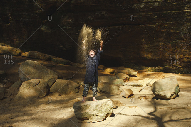 A small barefoot boy tosses golden sand in the air in a sunlit gorge