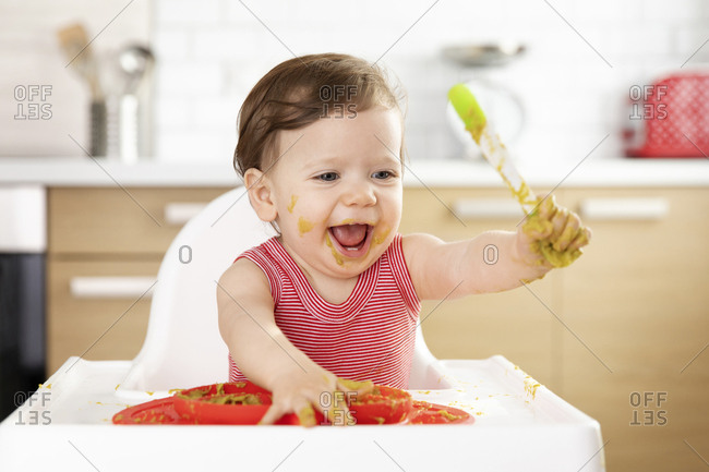 Happy baby in high chair eating pea puree with spoon