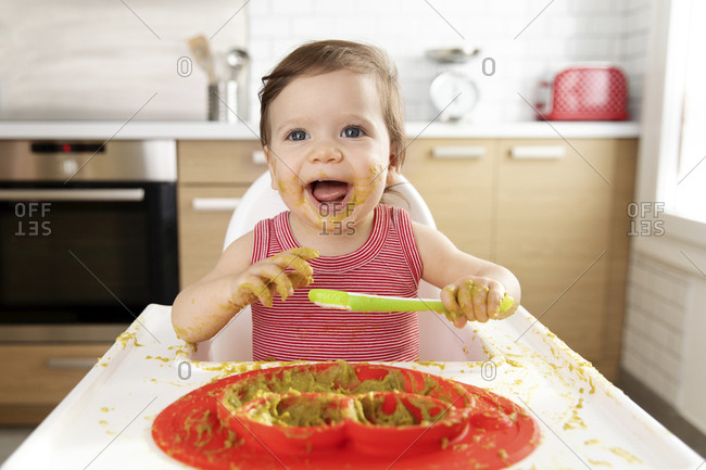 Happy baby in high chair making mess with pea puree
