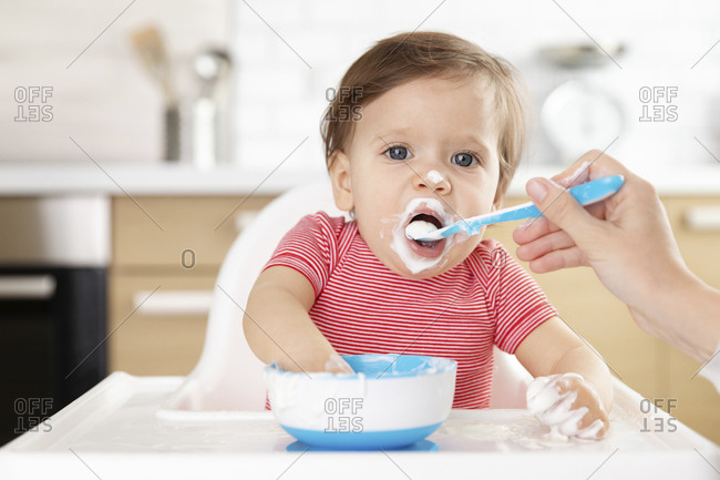 Baby sitting in high chair being fed with spoon