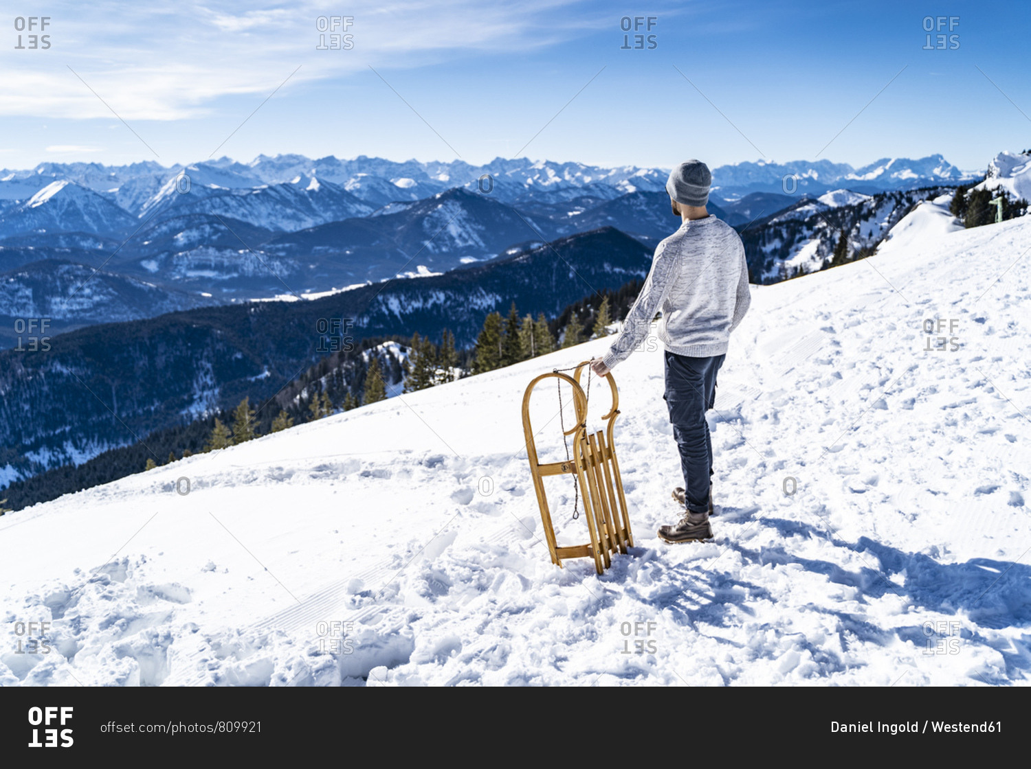 Germany- Bavaria- Brauneck- man with sledge in winter in the mountains looking at view