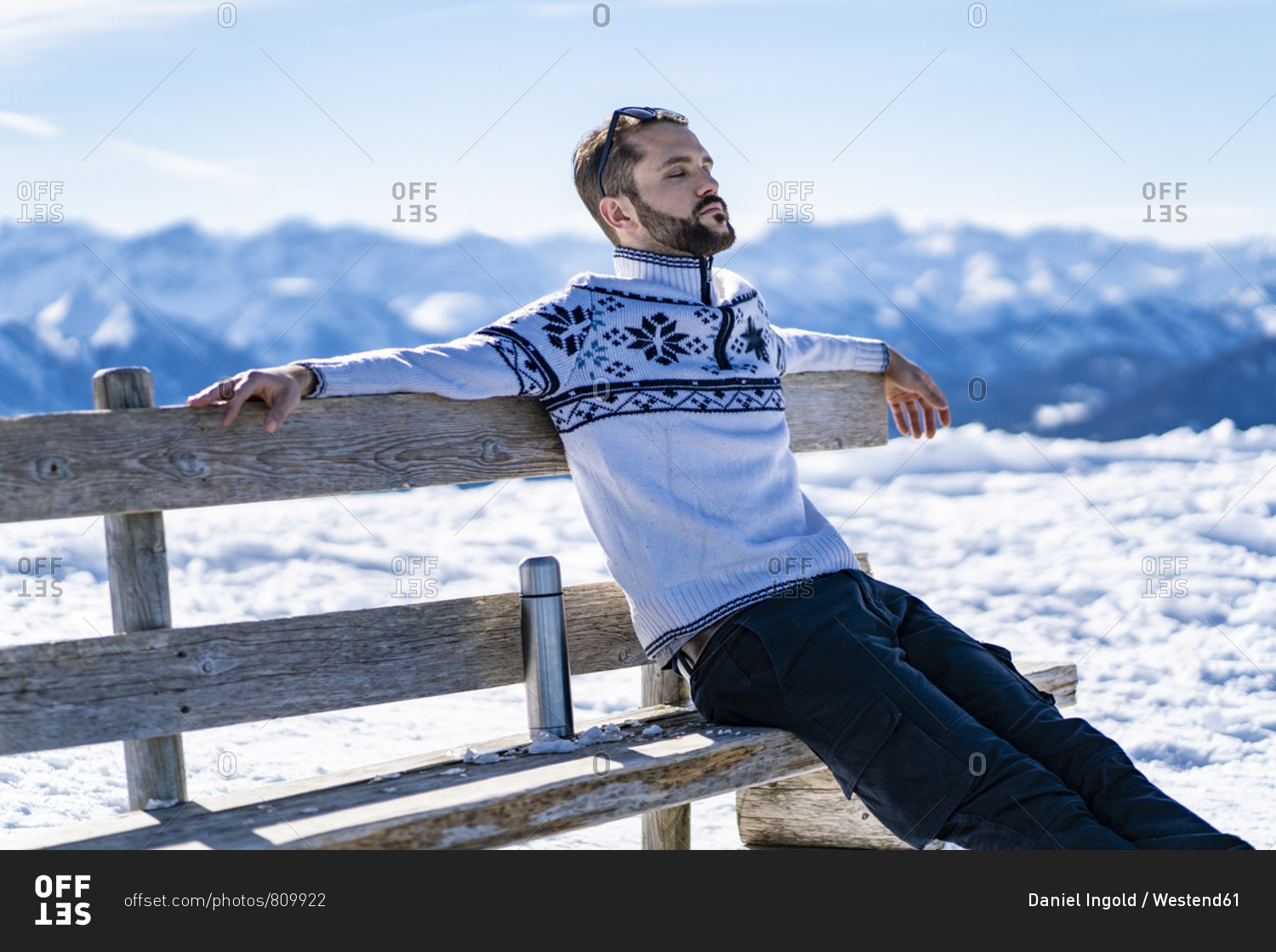 Germany- Bavaria- Brauneck- man sitting on bench in winter in the mountains having a break