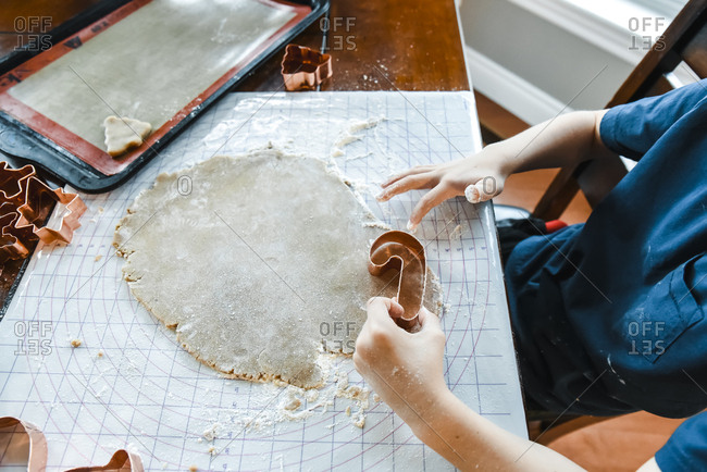 Close up of child's hands making cookies with cookie cutters.