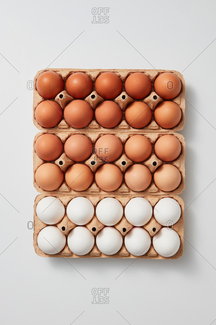 White and brown organic eggs in cardboard boxes presented on a gray background with space for text. Healthy product. Flat lay