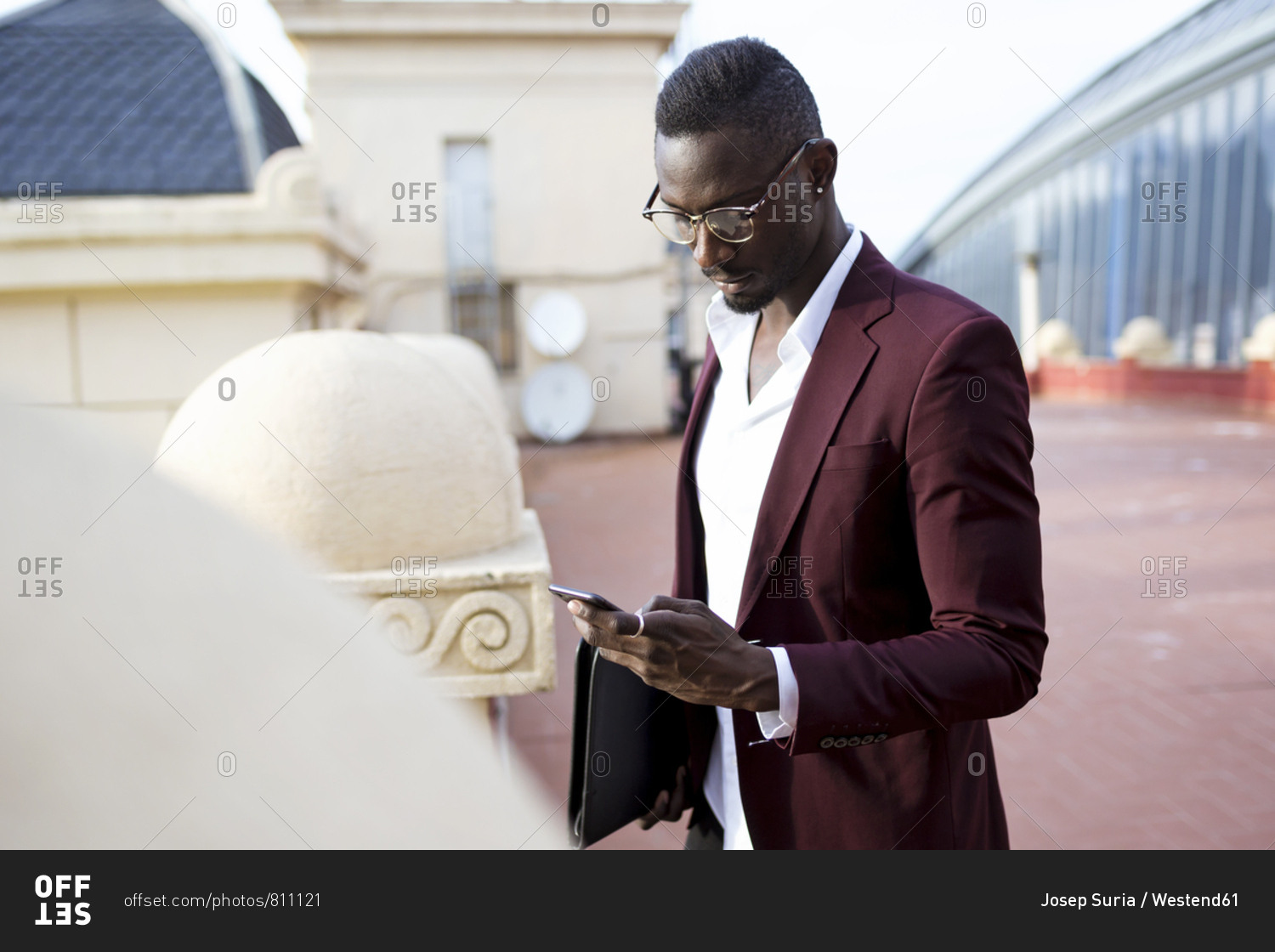 Young entrepreneur waiting on hotel terrace for his appointment- using smartphone