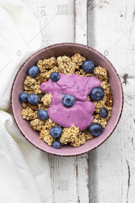 Granola with blueberries and blueberry yoghurt in bowl on white wood