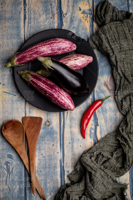 Set of fresh ripe eggplants placed near piece of striped cloth on weathered wooden tabletop
