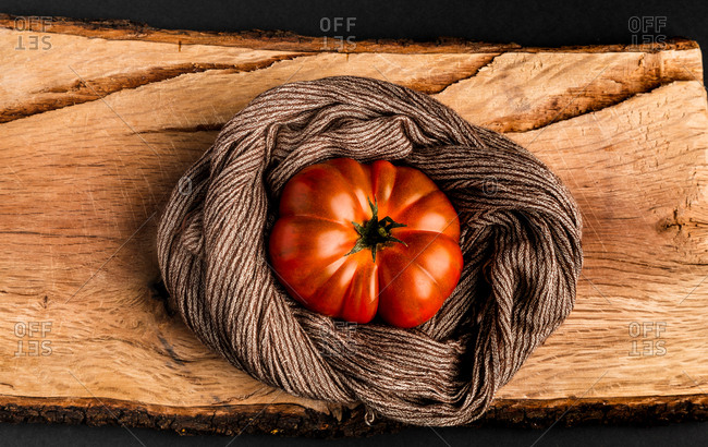 Fresh ripe tomato and fabric napkin placed on piece of wood against black background