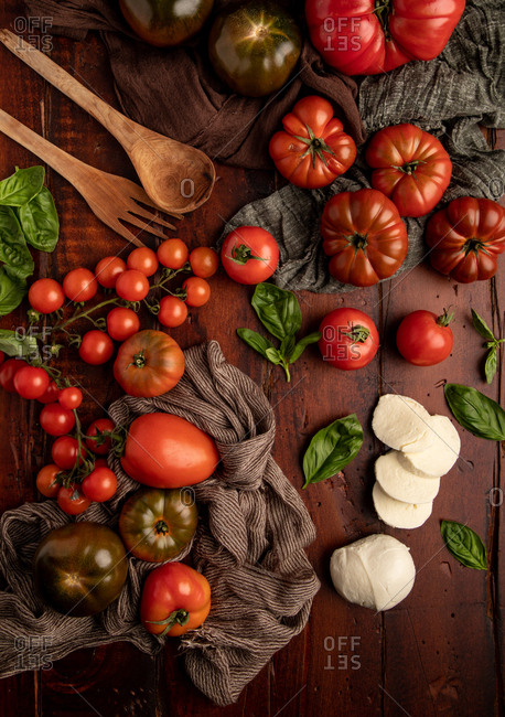 Fresh tomatoes and mozzarella cheese with basil leaves for salad placed on wooden board and fabric napkin