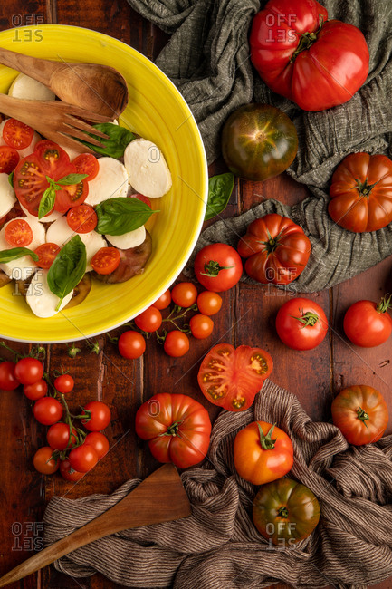 Fresh ripe tomatoes and cloth napkins placed on wooden tabletop near bowl of yummy Caprese salad