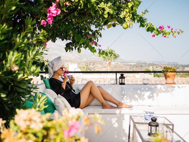 Chinese young rich woman in black satin dressing gown and towel in head resting in a balcony enjoying beautiful views on a sunny bright morning
