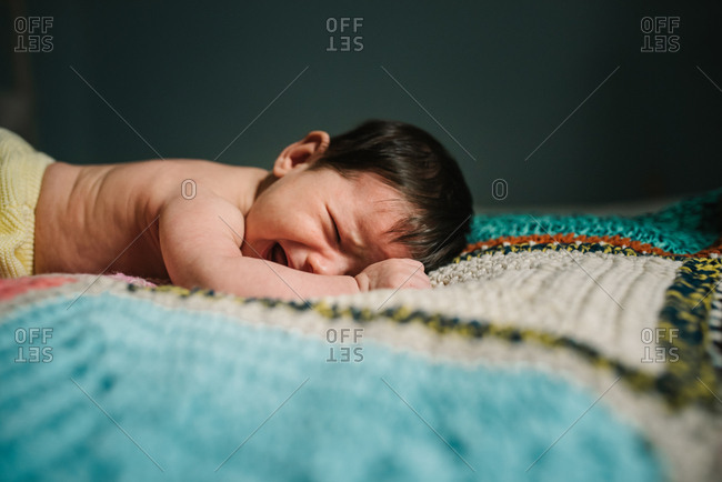Cute shirtless baby lying on warm knitted blanket and crying loudly in cozy nursery