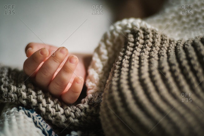 Close-up hand of anonymous sleeping baby lying under soft knitted blanket in nursery