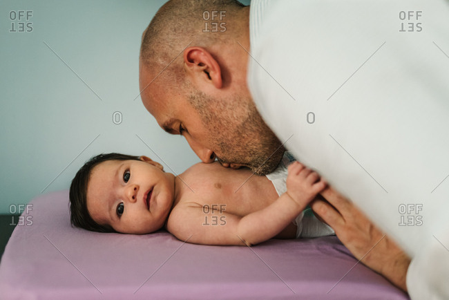 Bald adult man kissing adorable newborn baby in tummy at home