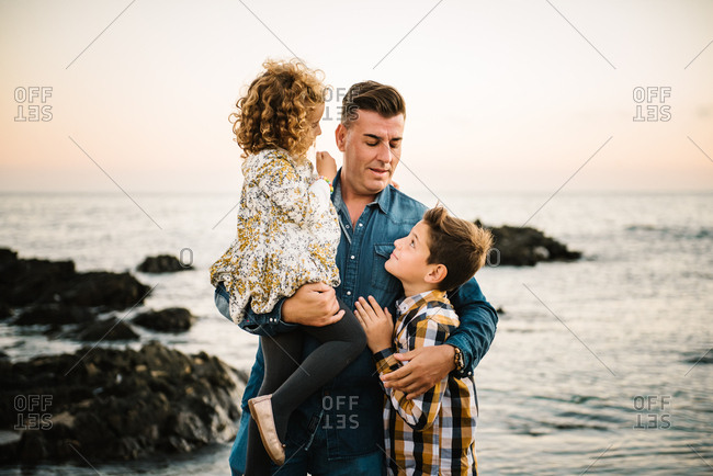 Middle aged man with her children at sea shore smiling and hugging each other