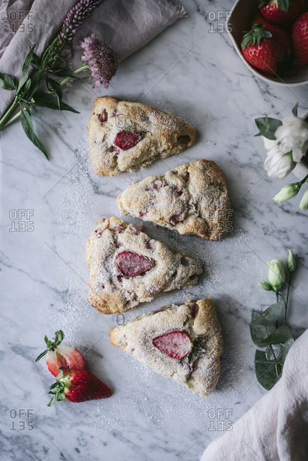 Set of delicious strawberry scones placed on white marble tabletop near flowers