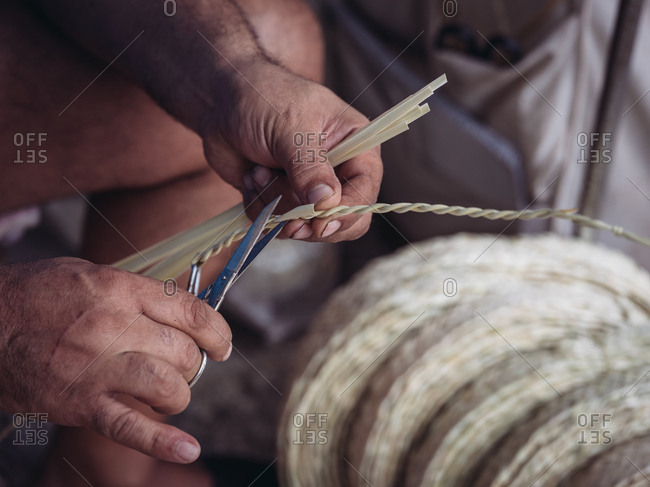 Hands of anonymous artisan showing lovely basket with floral ornament braided from dried palm fiber