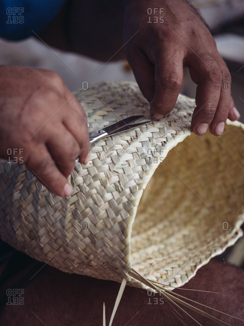 Hands of anonymous artisan showing lovely basket with floral ornament braided from dried palm fiber