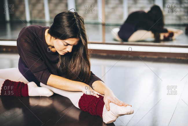 Girl practicing ballet and flexing muscles sitting on studio floor.