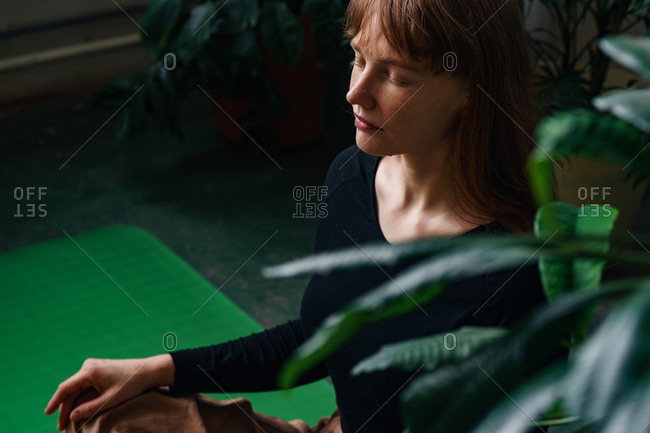 Profile of a young redheaded girl meditating in the room full of plants