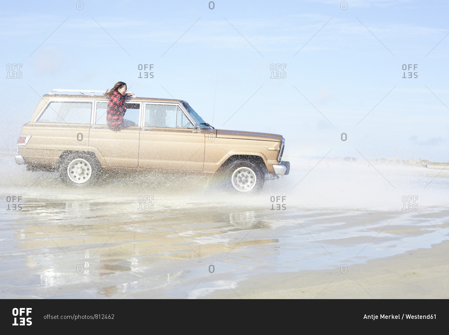 Germany- St Peter-Ording- girl leaning out of window of off-road vehicle driving through water on the beach