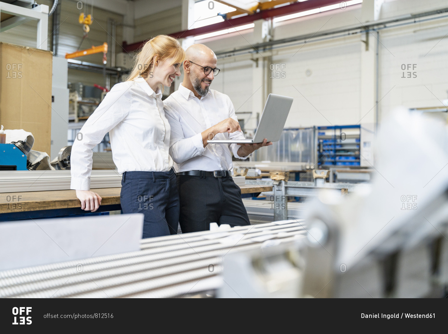 Smiling businessman and businesswoman using laptop in factory