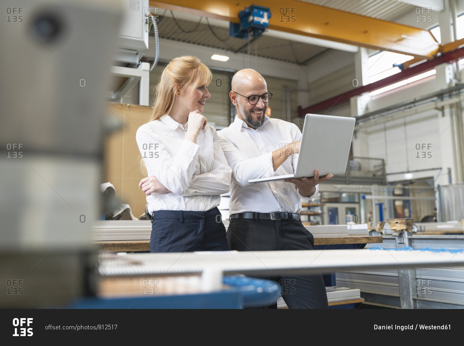 Smiling businessman and businesswoman using laptop in factory
