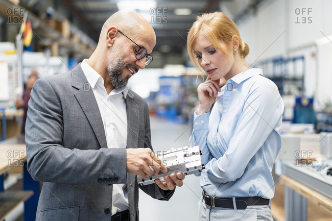Businessman and businesswoman examining work piece in factory