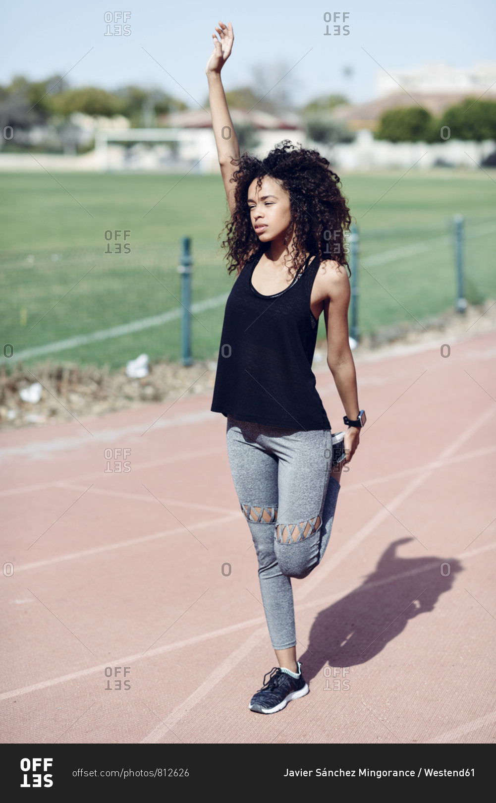 Sporty young woman stretching on tartan track