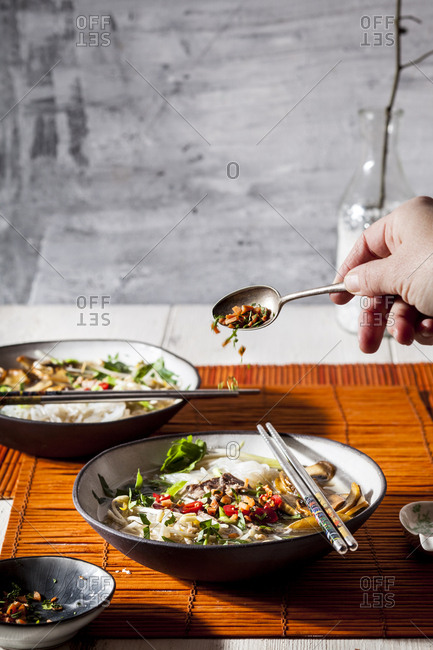 Woman's hand garnishing Vietnamese rice noodle soup