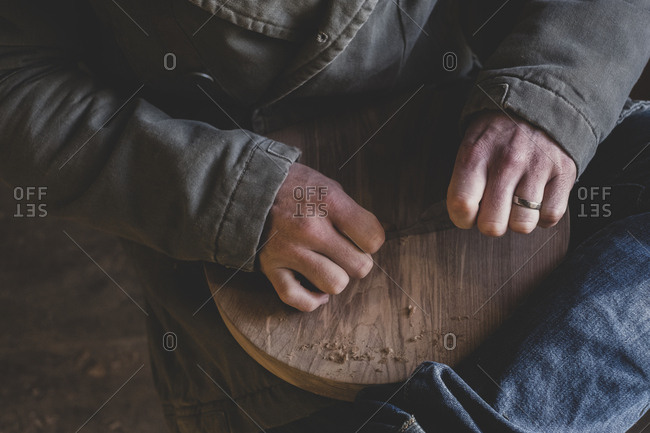 High angle close up of man sitting in workshop, holding piece of wood.