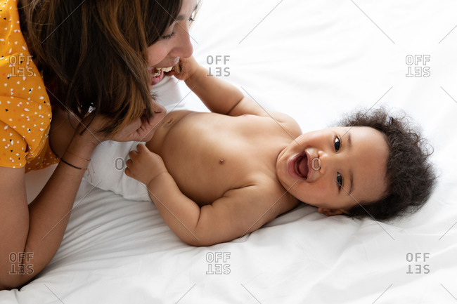 Smiling mother playing with laughing baby on bed