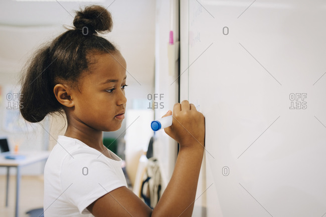 Schoolgirl writing on whiteboard at classroom