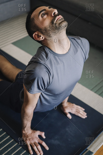 Young adult man practicing yoga in living room at home.