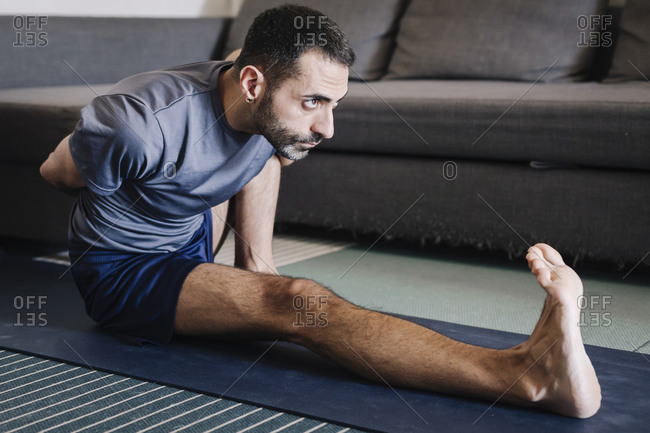 Young adult man practicing yoga in living room at home.