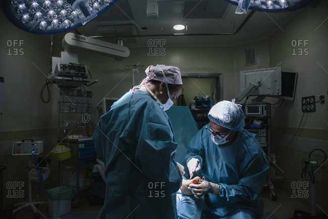 General view of the operating room with surgeon and assistant, the surgeon placing a screw on the patient's foot