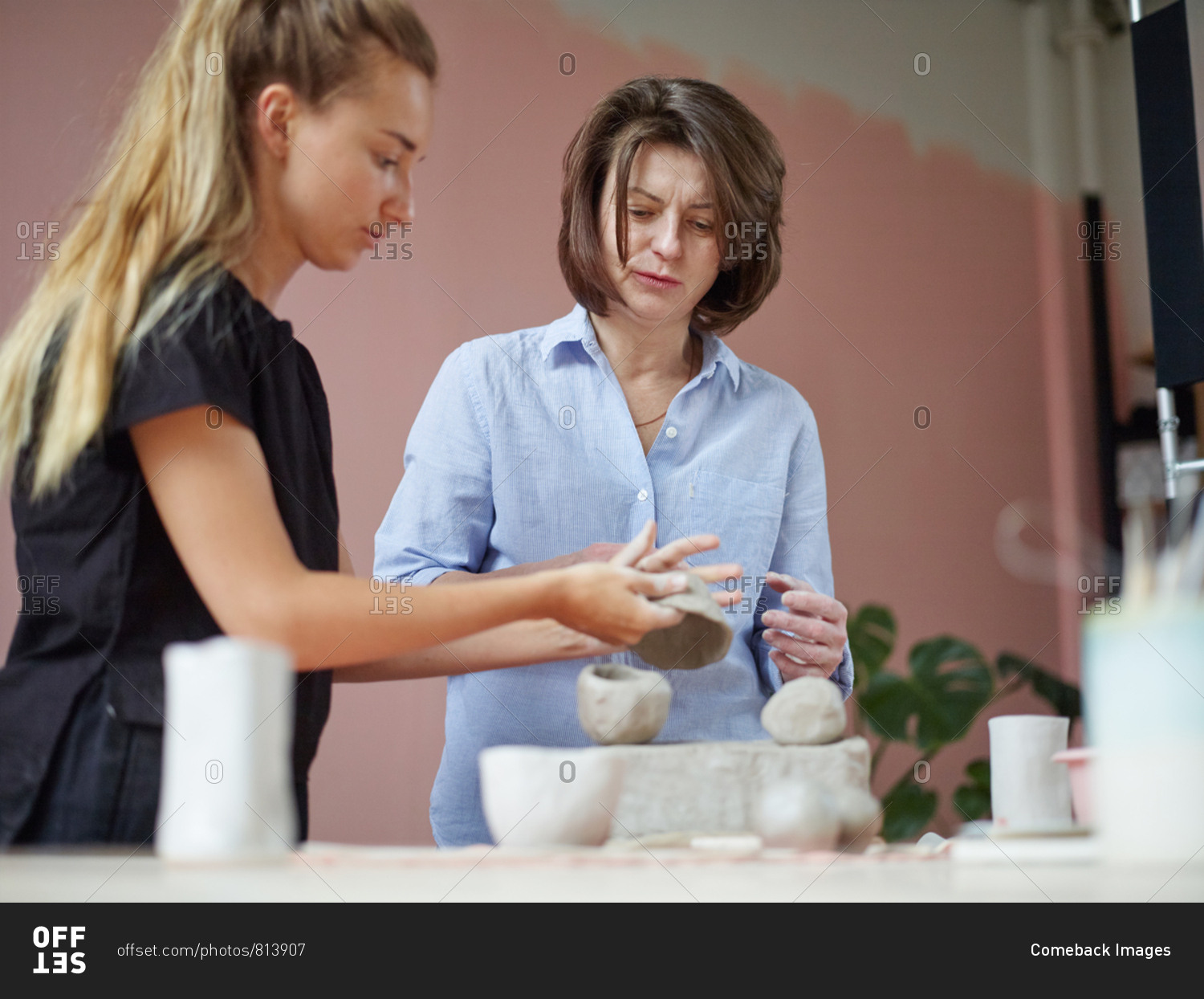 Young ceramic art teacher showing mature female student how to make clay bowl during personal class in art studio