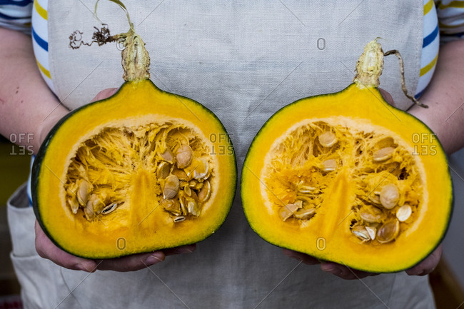 Close up of person holding pumpkin with orange flesh cut in half.