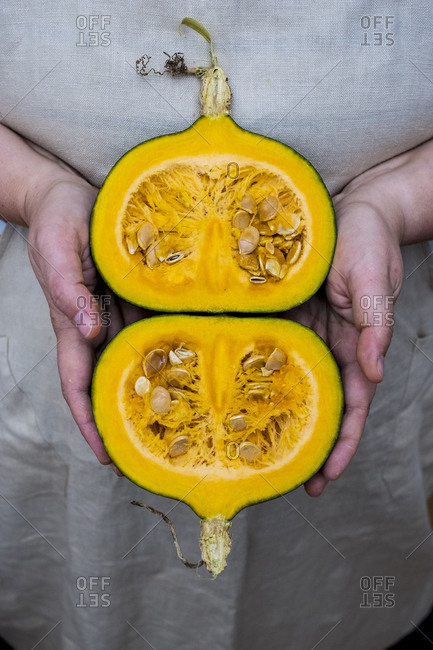 Close up of person holding pumpkin with orange flesh cut in half.