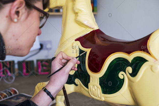 Close up of woman in workshop, painting traditional wooden carousel horse from merry-go-round.