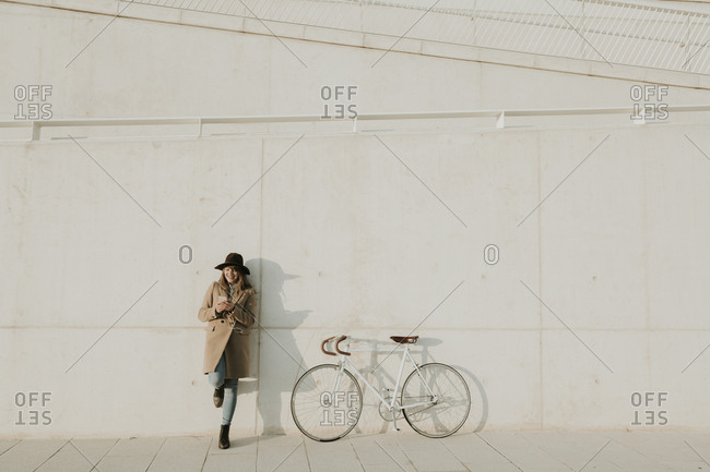 Young hipster woman leaning next to a bicycle- holding a phone